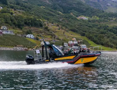 Boat speeding through the water, with a grassy hill in the background