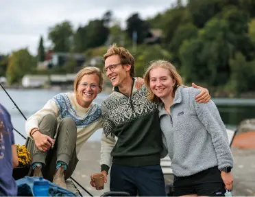 One man and two women with arms around their shoulders, smiling with a large lake behind them