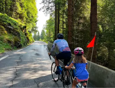 Father and daughter biking  on a road using a trailer bike