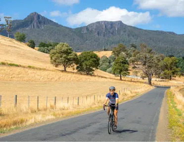 Person biking on a road with dried field patches on both sides