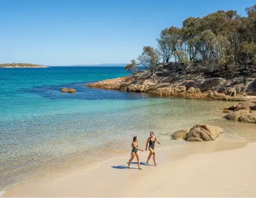 Two woman smiling at each other while walking on a beach