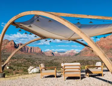 Outdoor lounge area with cushioned seating beneath a modern canopy structure, overlooking Zion’s red rock mesas, cliffs, and expansive desert landscape under a bright blue sky with scattered clouds.