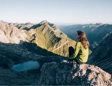 Woman sitting on top of a cliff looking down towards a valley