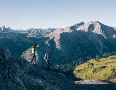 Two people descending down a mountain, with larger mountains in the distance
