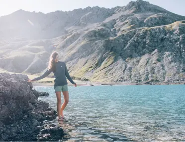 Woman standing on a rock next to a large lake and mountains