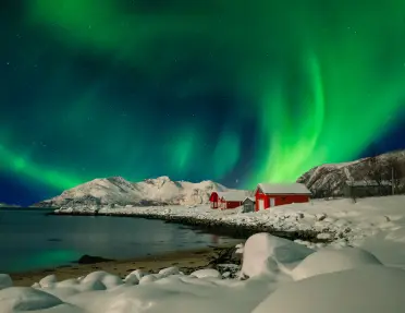 Aurora over a snowy field with two red barns