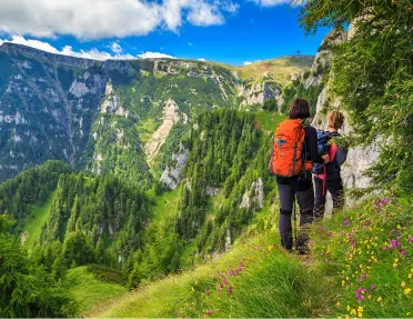 Two people walking on a grassy trail, with views of tall mountains