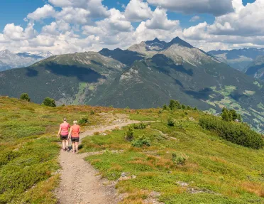 Two women hiking on a trail with mountains and clouds in the distance