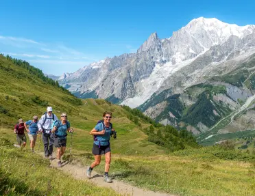 Group of people running on a grassy trail, with large mountains in the distance
