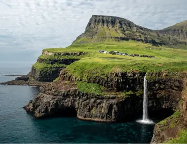 Large, grassy cliff with a waterfall and the ocean below