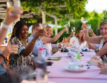 Group of friends holding up their drinks while dining at a violet table in Italy.