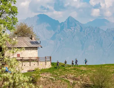 Hikers walk towards a stone home with a mountain range in the background.