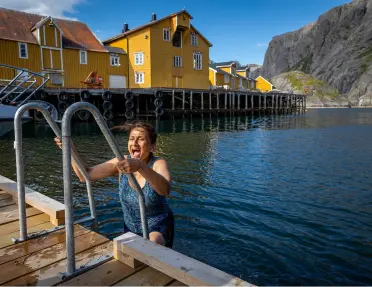 A woman using a swim ladder to exit the water after a swim in Nusfjord, Norway.