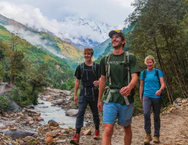 Two men and one woman walking along a frozen river with a forest in the background