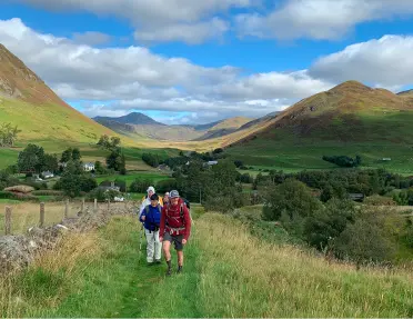Group of people hiking through a grassy field, with views of large hills in the distance