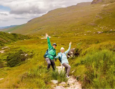 Man and woman smiling with their arms open, in the middle of a trail in the valley