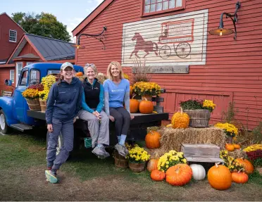 A family sits on a vintage blue truck surrounded by pumpkins and yellow flowers at the Vermont Country Store in Rockingham, Vermont.