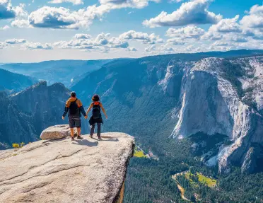 A couple hold hands while looking down into Yosemite Valley and El Capitan.