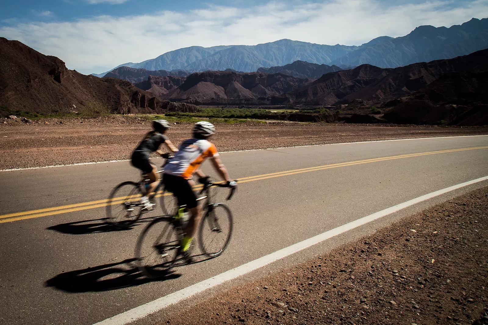 Two guests biking down arid, rocky road. dark rock hills in background.