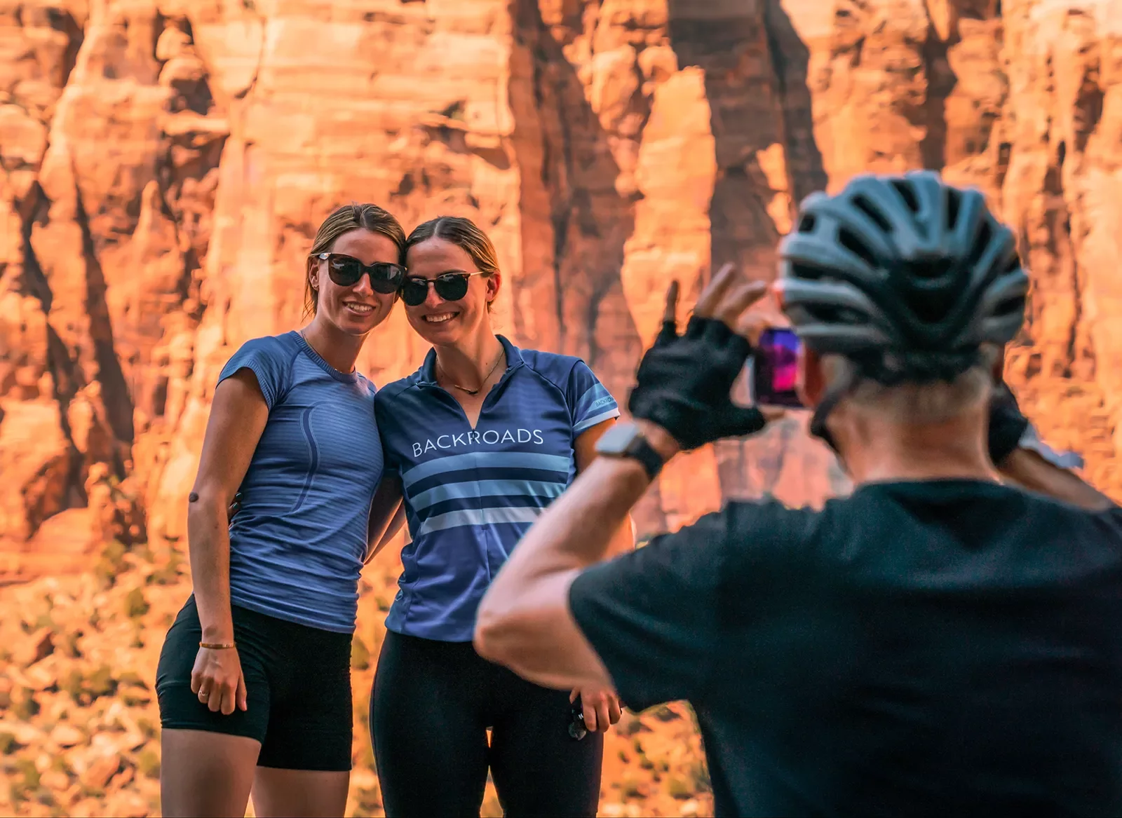 Guest taking photo of two others, all in bike gear, orange cliffs behind them.