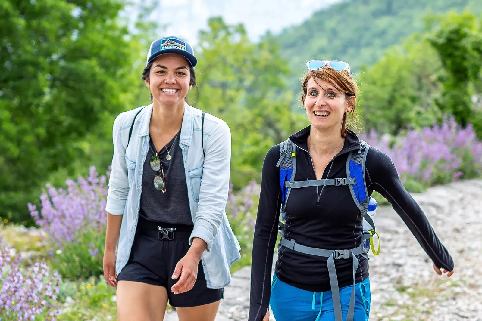 Two hikers on a trail with wildflowers.