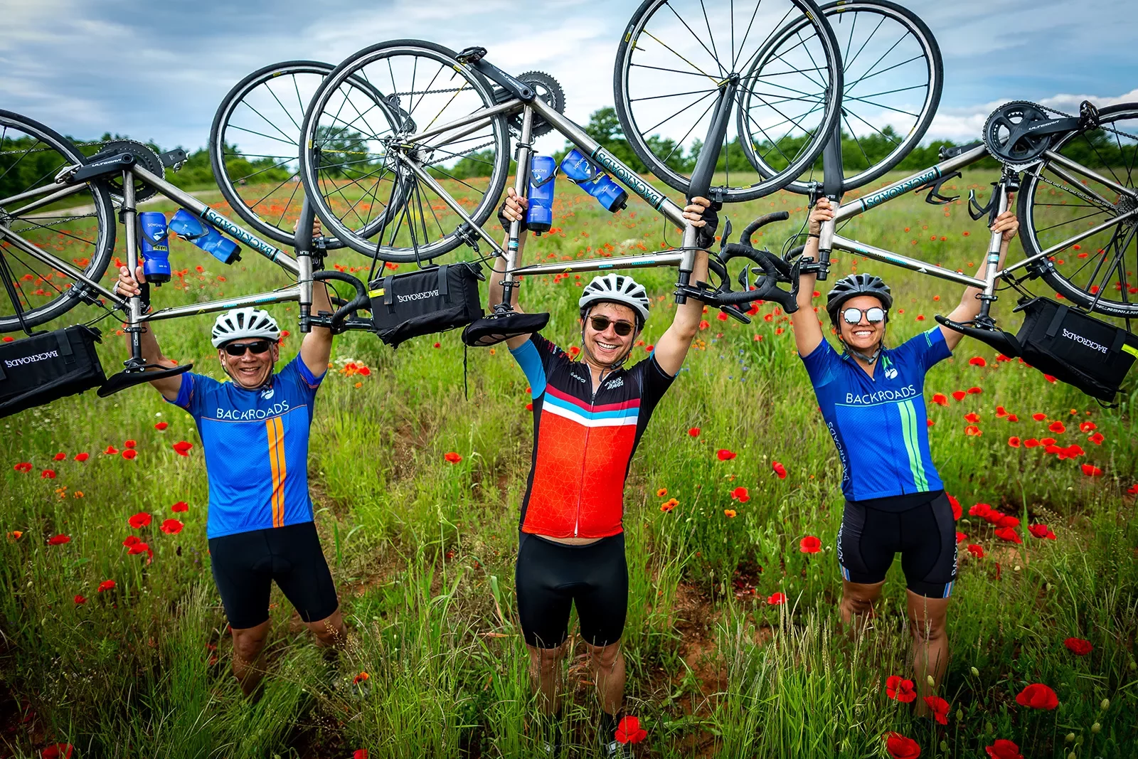 Three guests in flower field holding bikes over their heads.