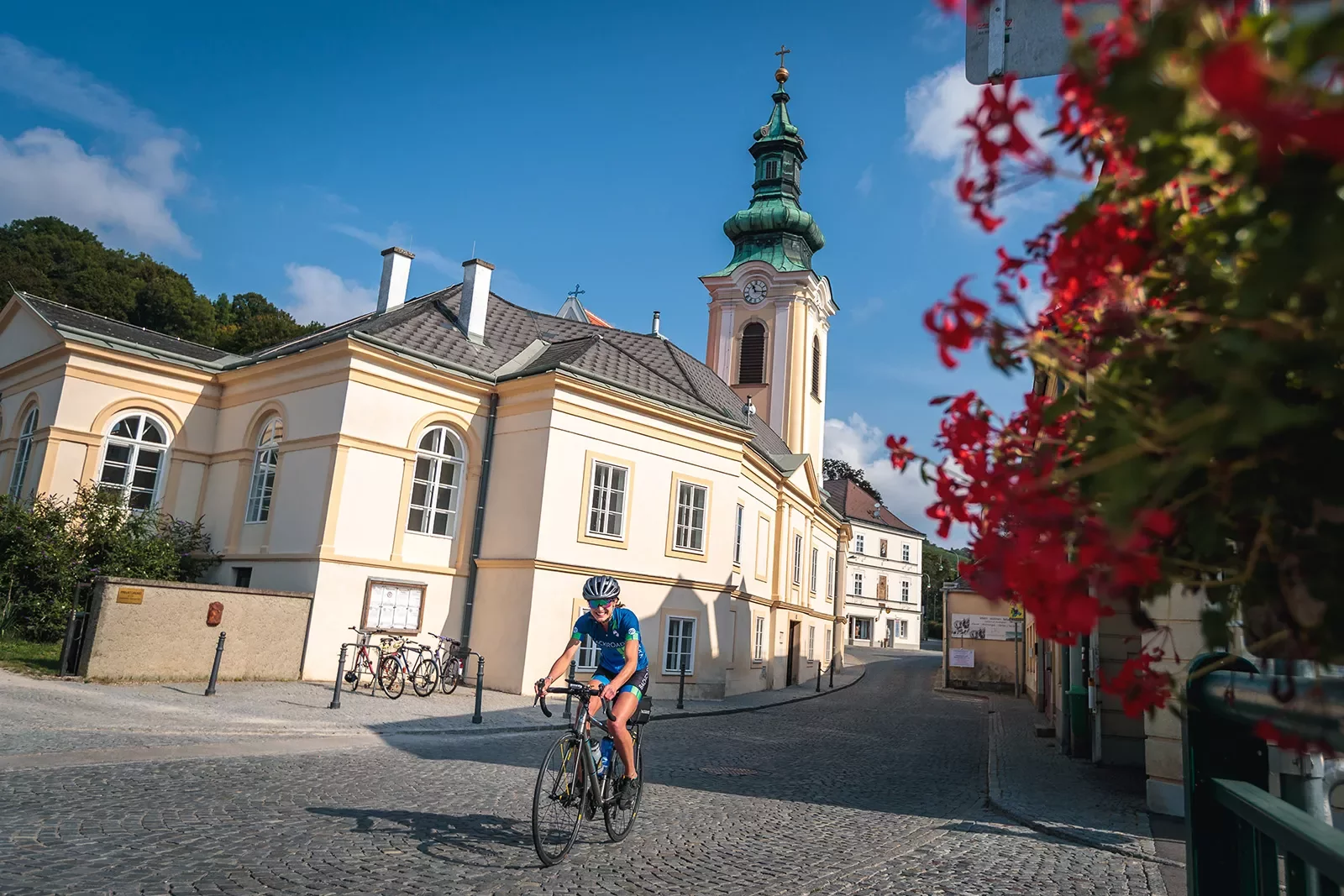 Biker riding past clock tower on cobblestones in Europe.