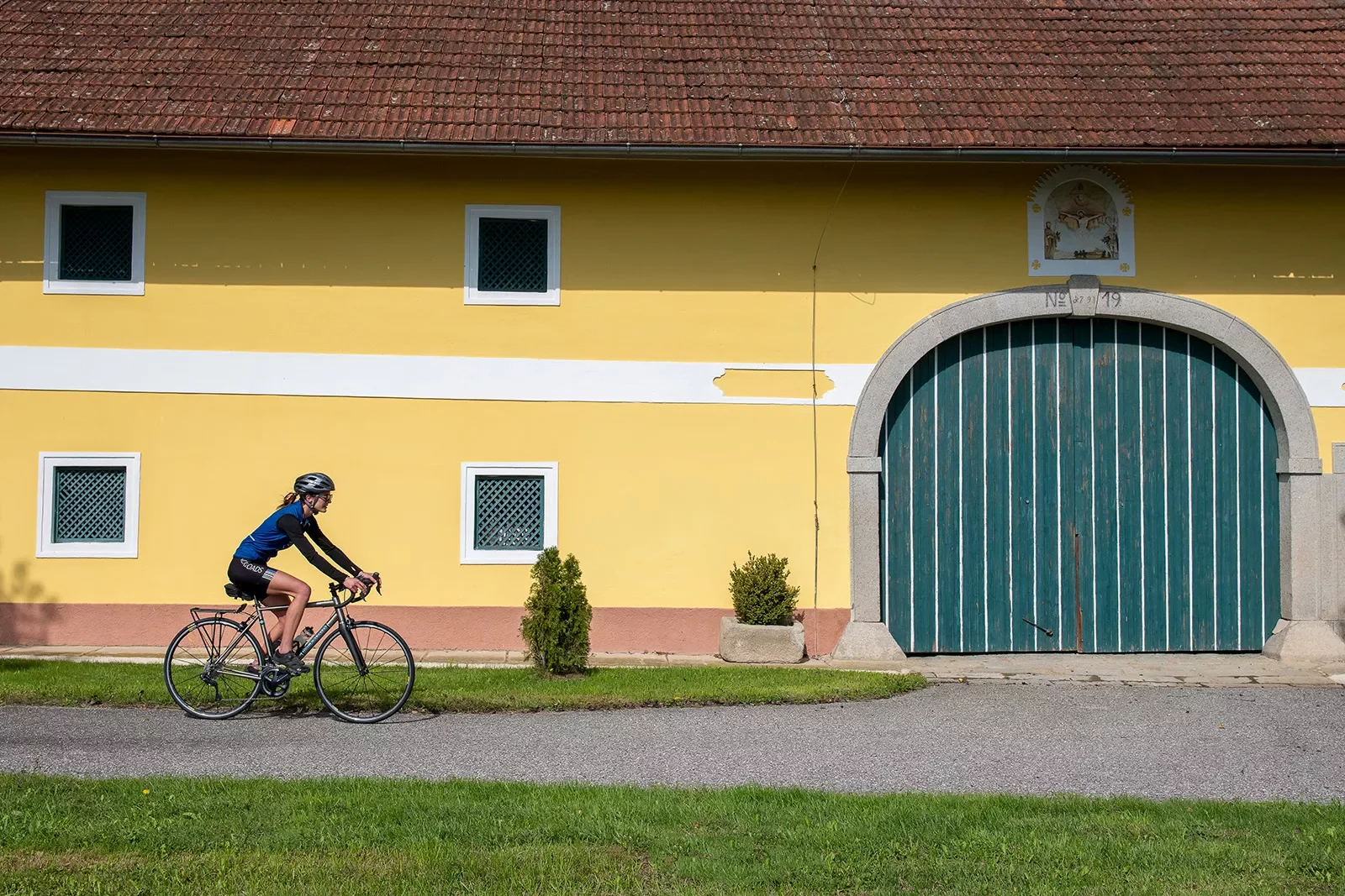 Biker riding past a bright yellow building at noon.