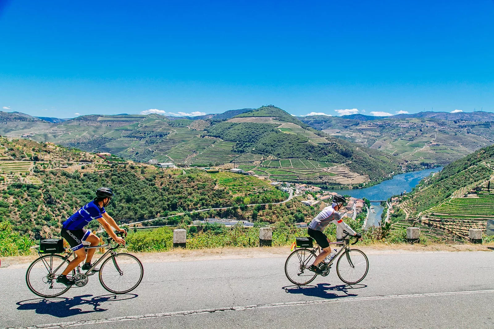 Two bikers riding on a road along the Douro River.