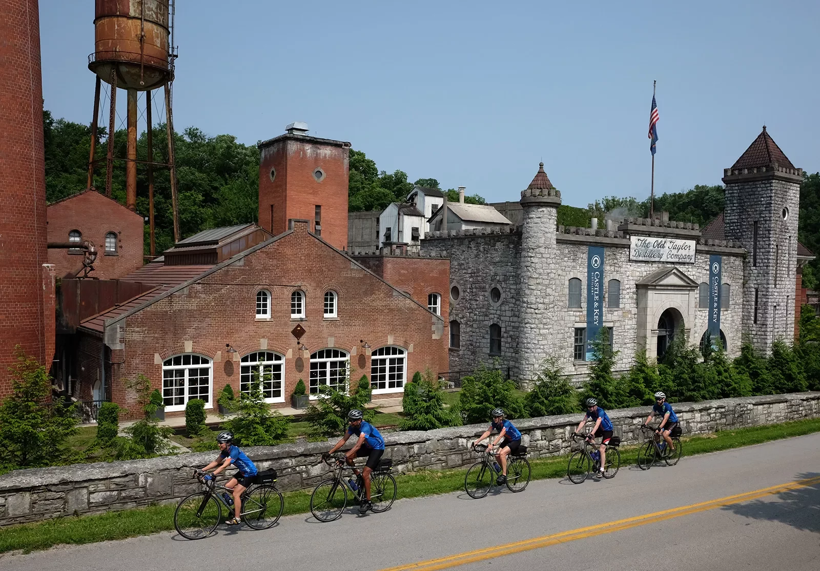 Five guests cycling past the &quot;OLD TAYLOR DISTILLERY COMPANY&quot; and it's brick buildings.