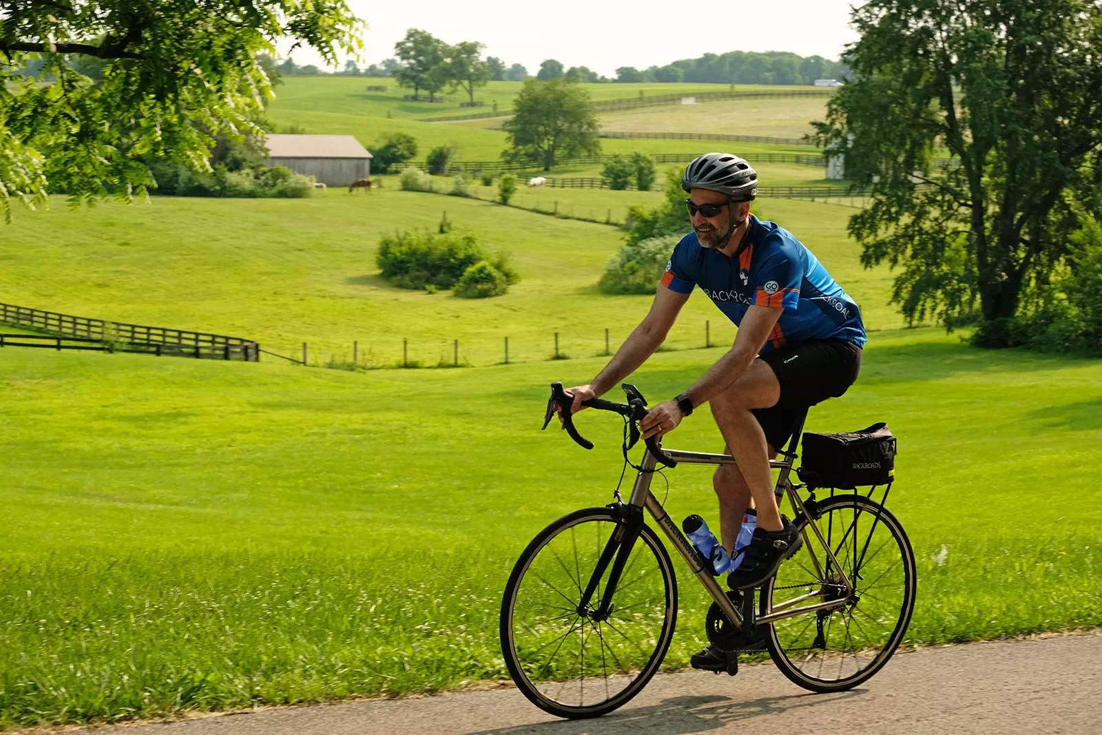 Guest cycling past farmhouses, grassy meadow.
