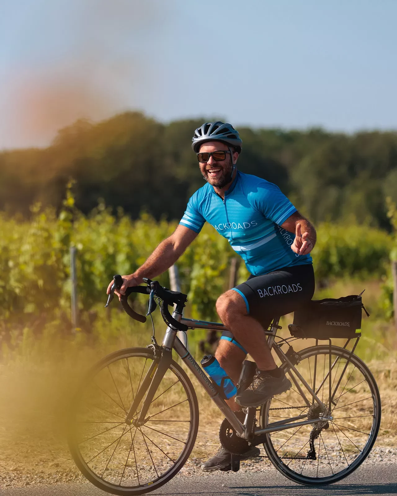 Guest cycling past grapevines, showing peace sign to camera.
