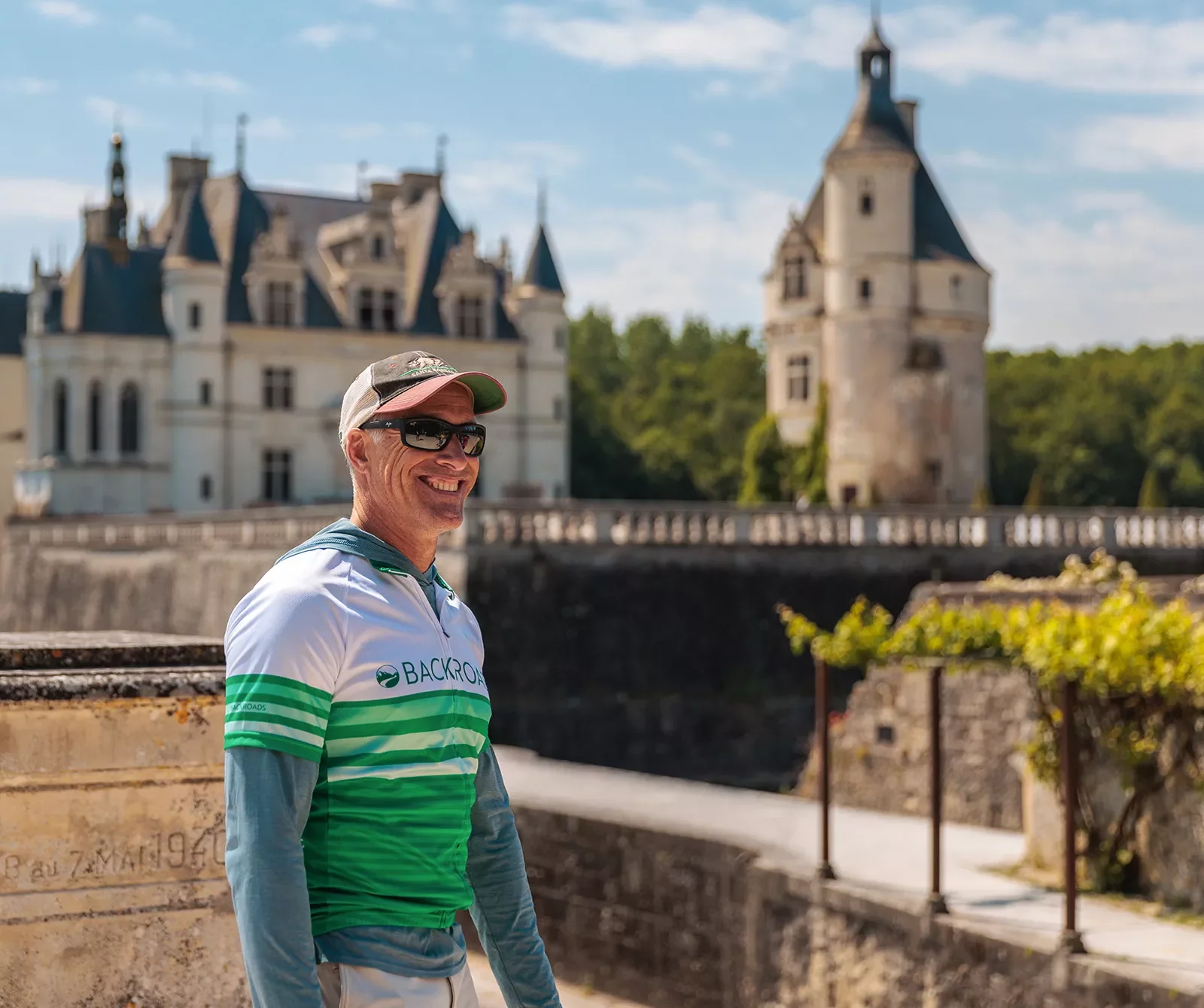 Guest smiling with green and white French chateau behind.