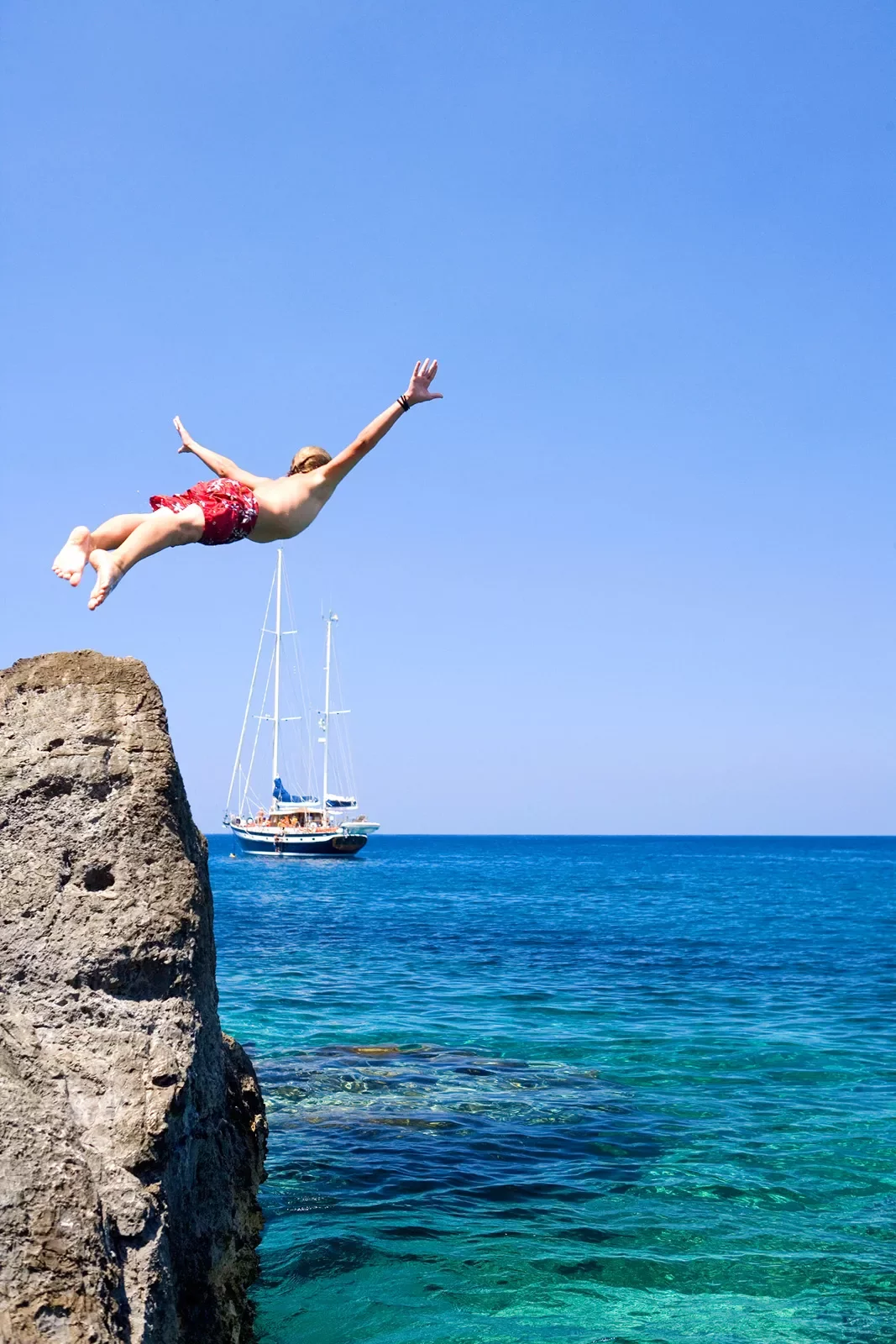 Swimmer diving off of a cliff into crystal clear waters.