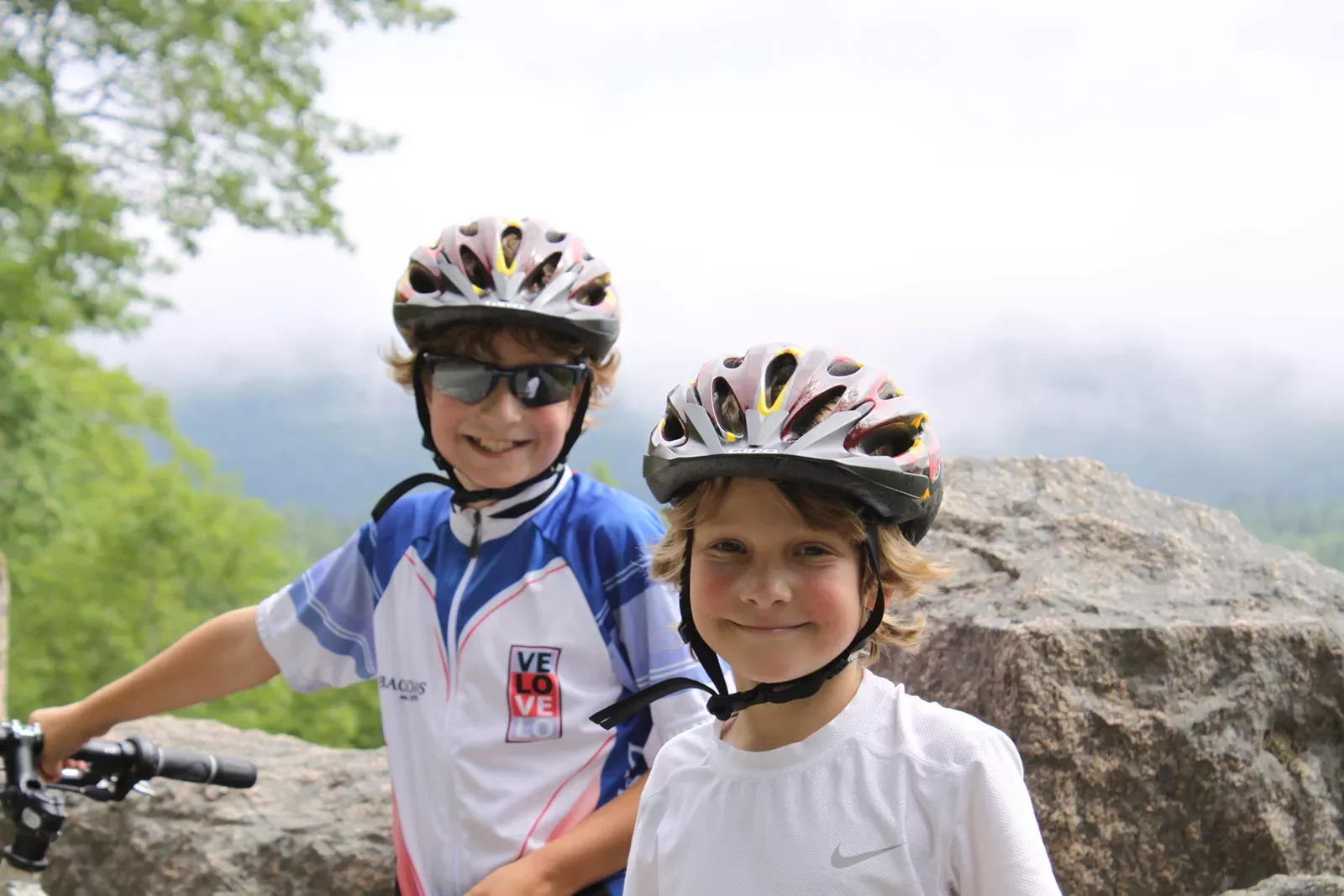 Two child guests in helmets smiling for camera, foggy vista behind them.