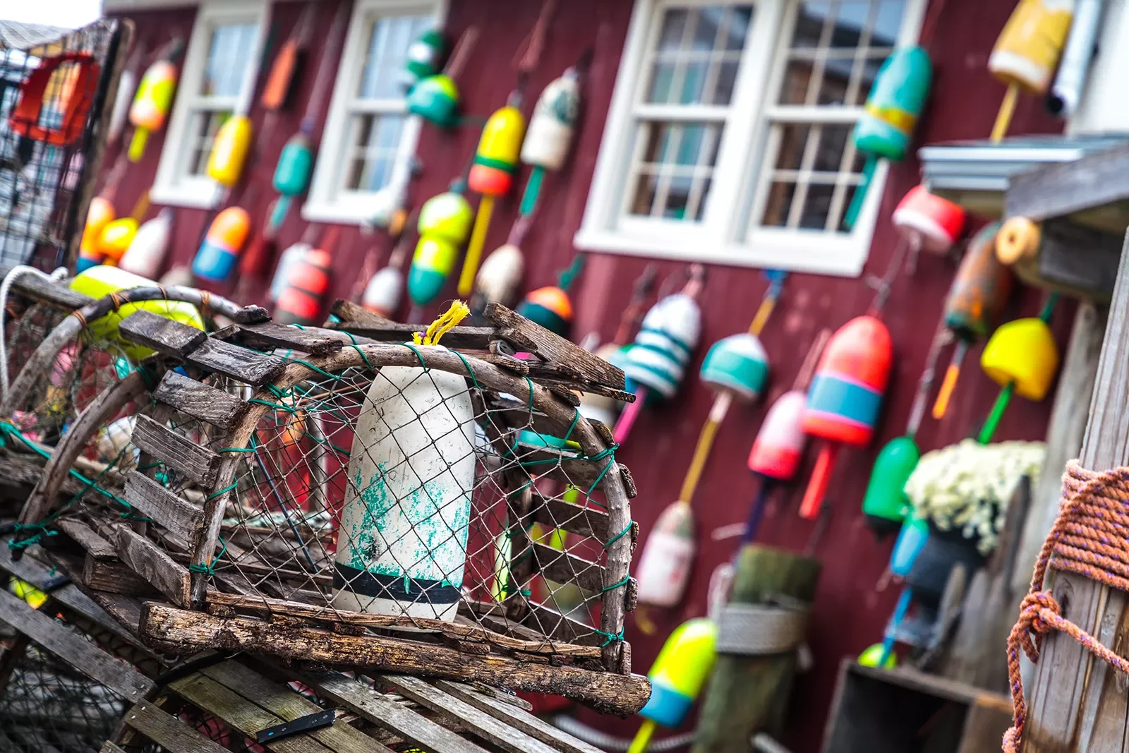 Shot of lobster trap in front of red fishing shack.