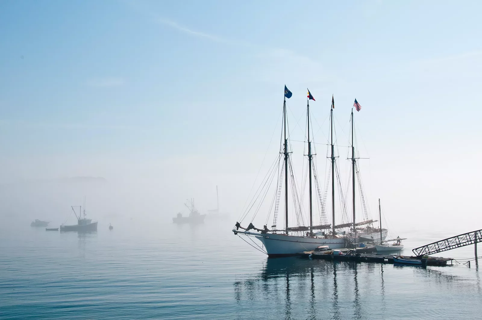 Wide shot of a four-masted ship in port, fog on the horizon.