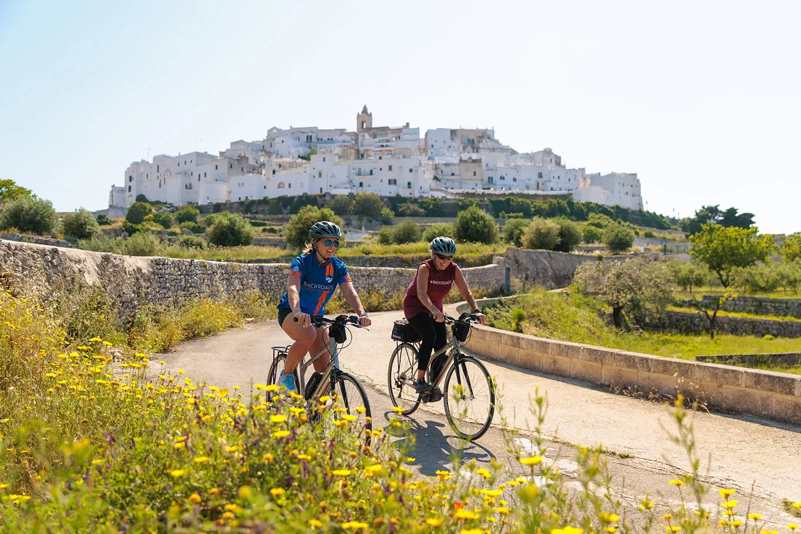 Two guests cycling in front of Ostuni hilltop.