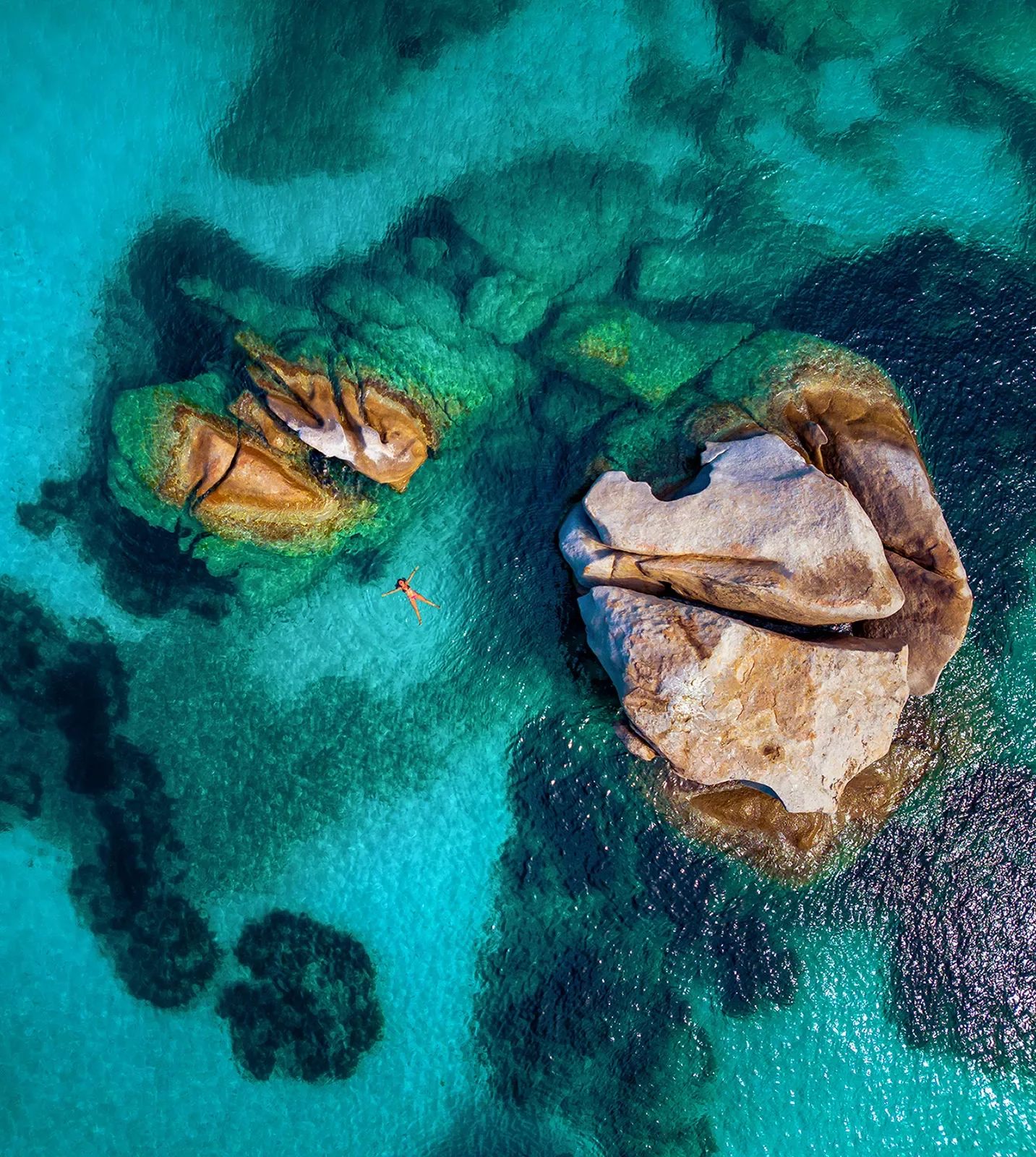 Overhead shot of guest swimming, light blue water, two large rocks.