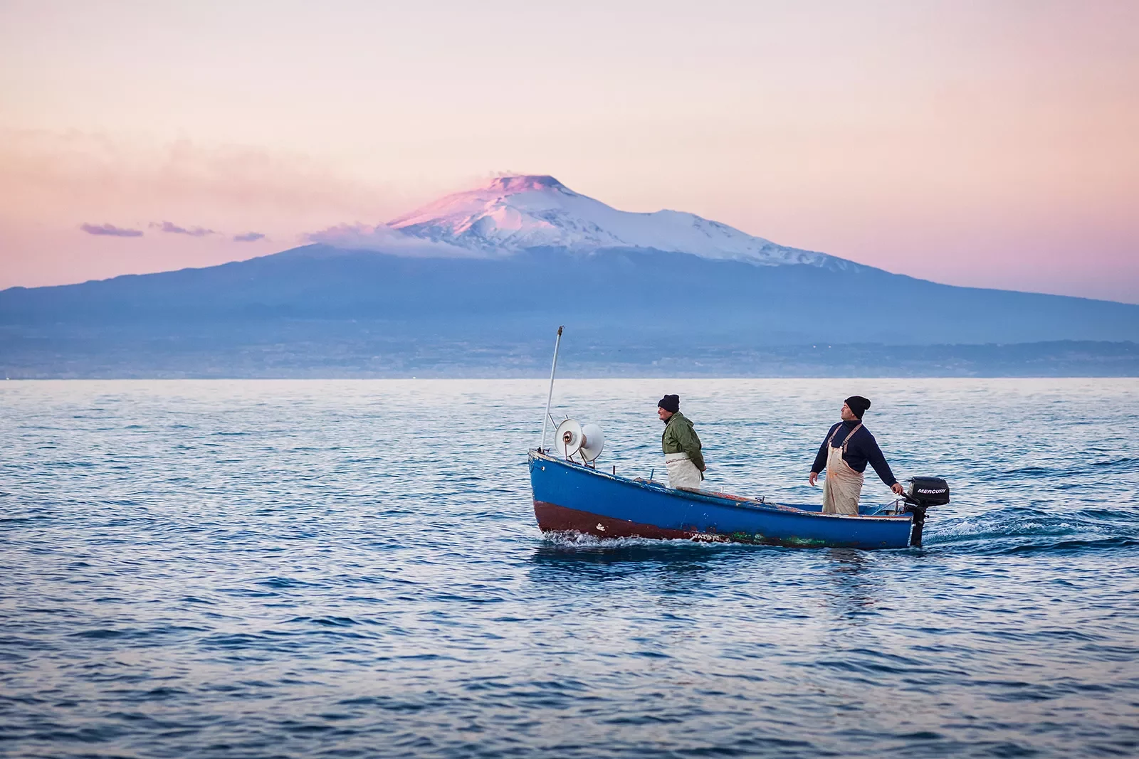 Two locals on boat during sunset, large mountain in distance.