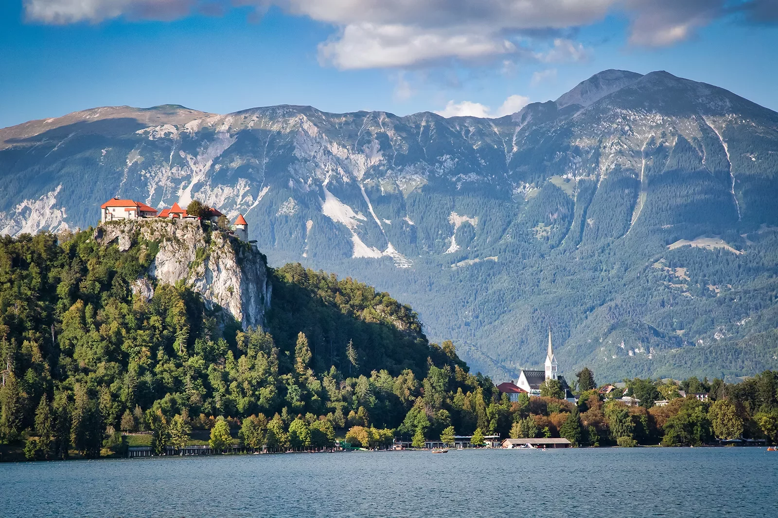 Wide shot of Bled Castle, town, lake below, mountain behind.