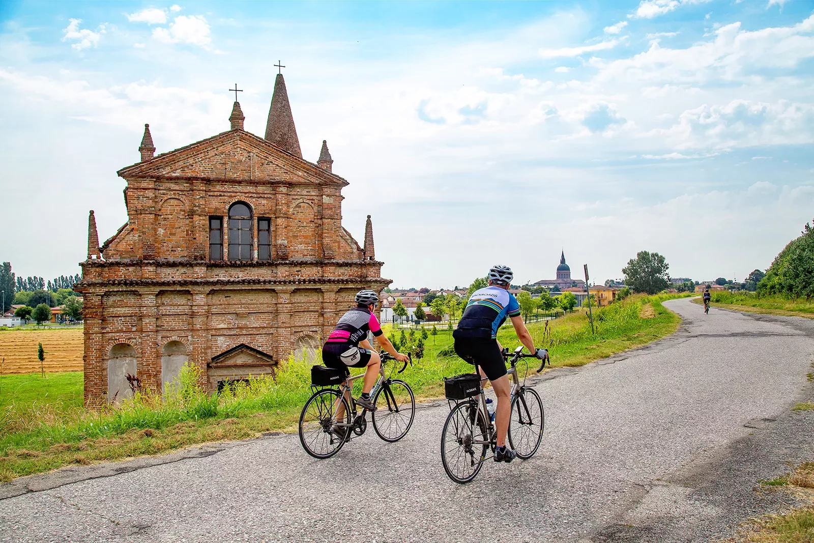 Cyclists riding along an Italian road with an old church building