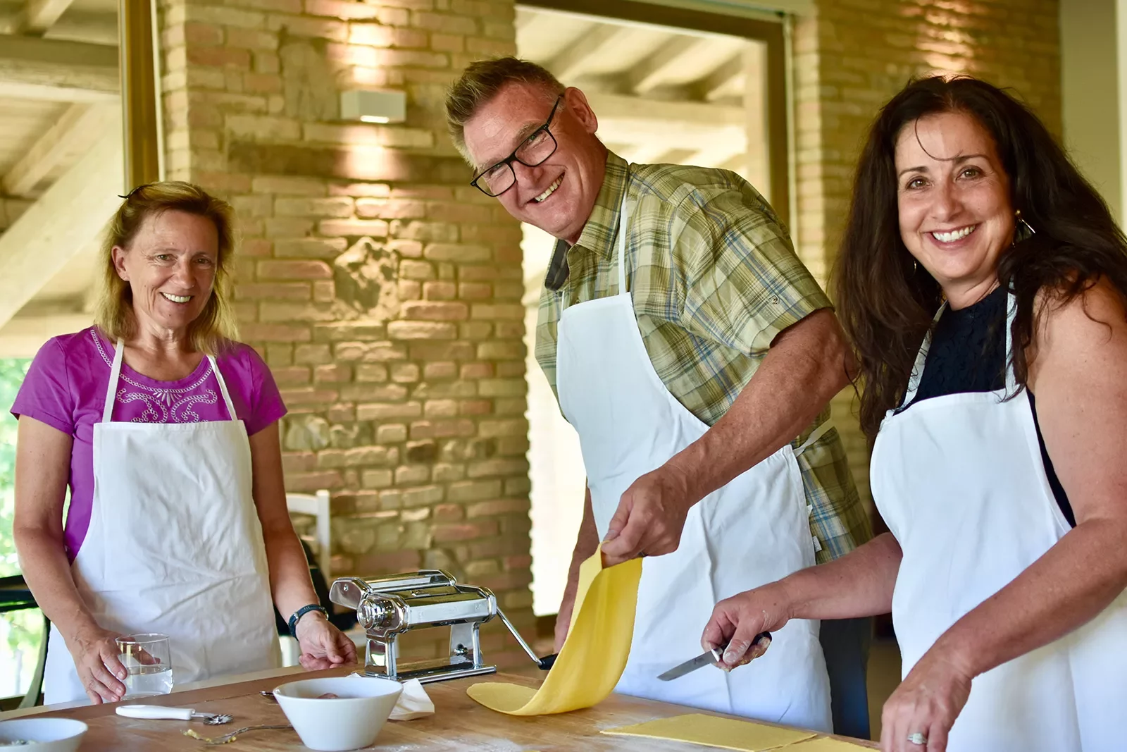 People smiling at the camera while rolling out pasta dough