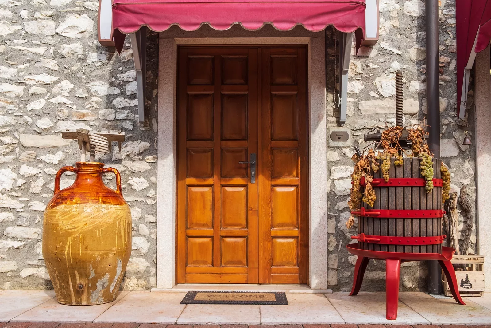 Stone storefront, large ceramic vase, wine grape crusher, wood door.