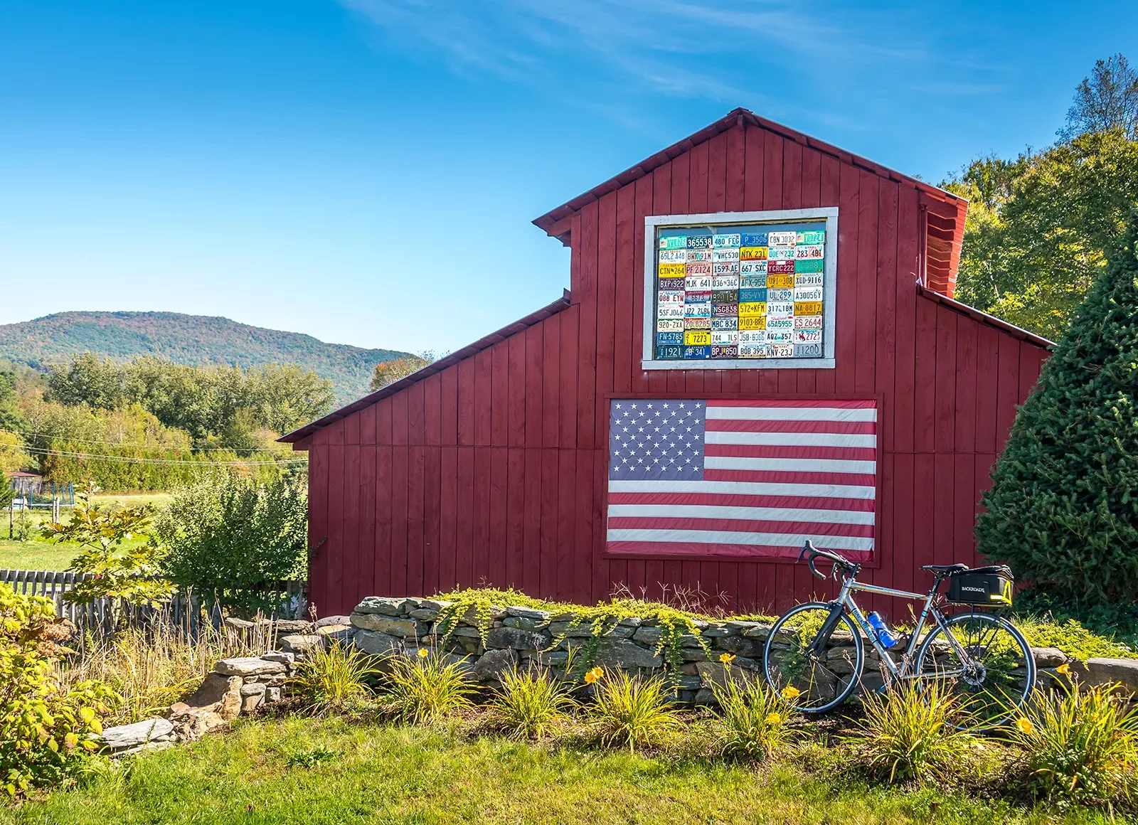 Shot of bike in front of red barn, US flag on barn wall.