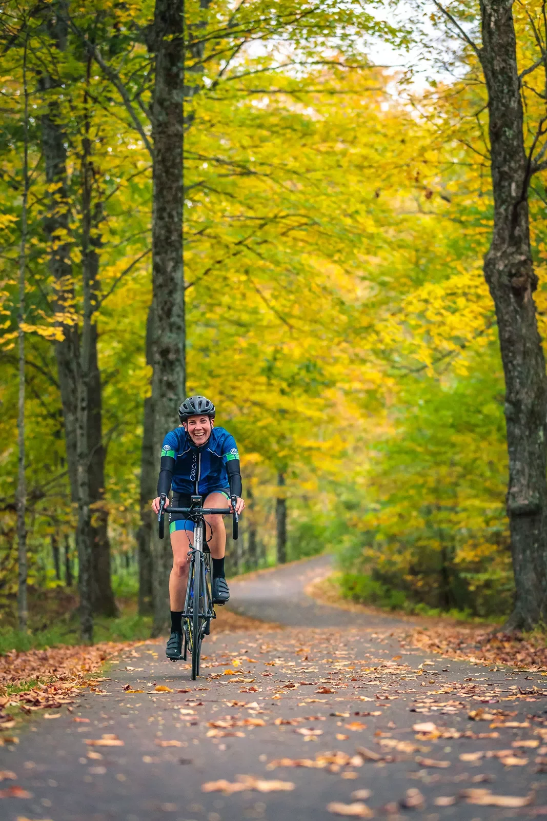 Guest cycling down fall road, facing camera and smiling.