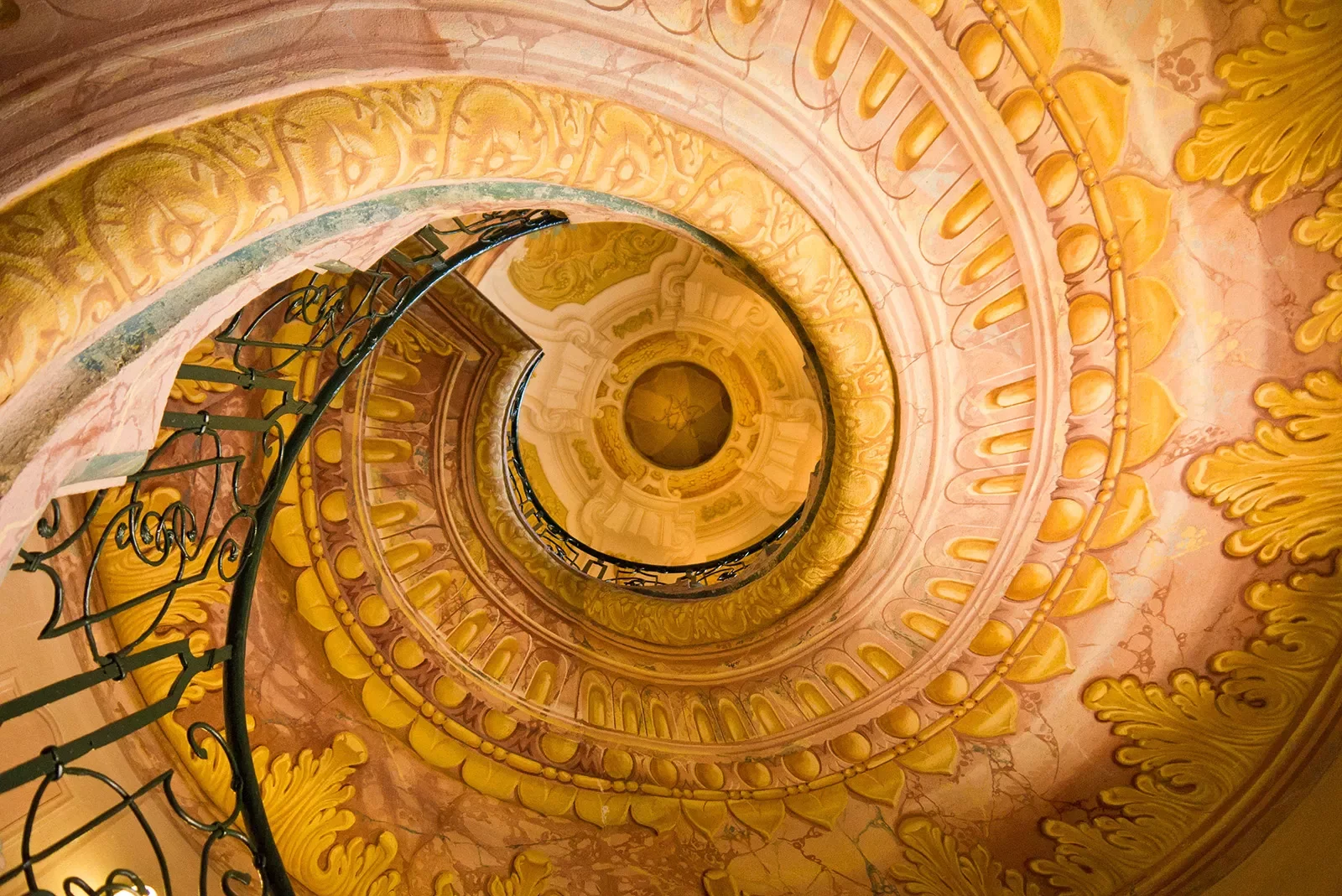 Ornate yellow and golden painted staircase spiraling to the ceiling.
