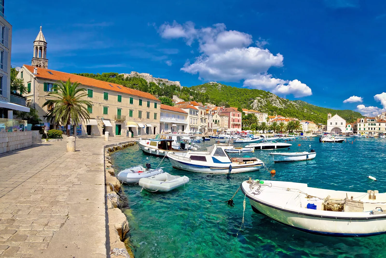 Wide shot of Croatian coastal town, boats, blue water, hills, etc.