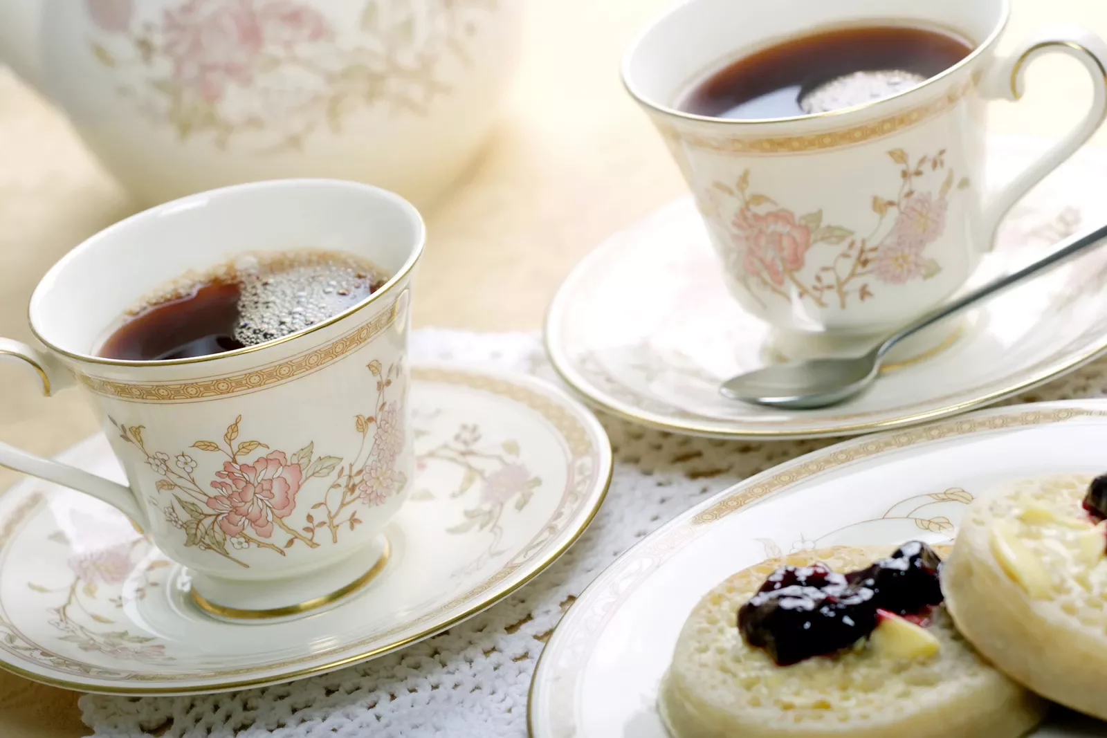 Ornate English cups of tea and english muffins with butter and jam.