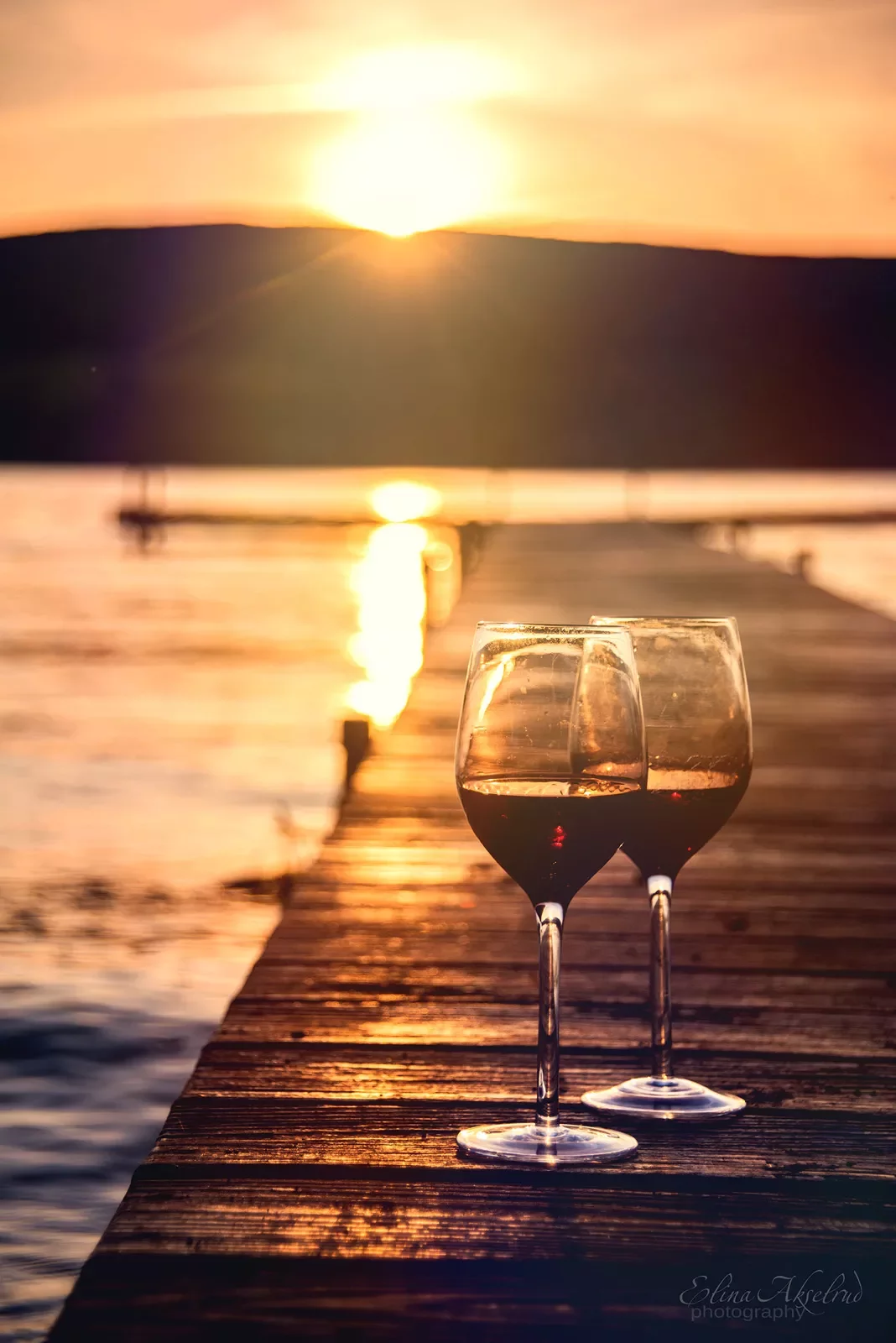 Two wine glasses sitting on pier, sunset in background.